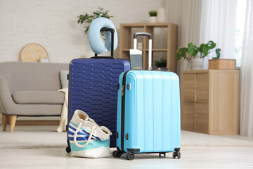Packed suitcases with neck pillow and beach bag in interior of living room