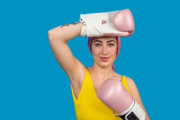 Young woman wearing boxing gloves and pink headscarf posing on blue background