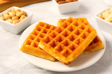 Plate with tasty Belgian waffles and bowls of different nuts on grey background