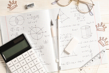 Copybook with handwritten maths formulas, calculator and stationery on white wooden background