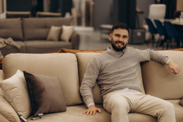 Fototapeta premium Smiling Man Posing Comfortably On Sofa in Modern Furniture Showroom