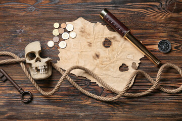 Burnt paper with skull, compass, coins and rope on wooden background. Pirate concept