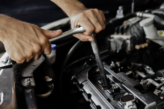 Close-up of male mechanic hand holding wrench for unscrewing to check or replace spark plug inside engine compartment at garage. Repair and maintenance concept.