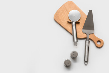 Wooden board with steel spatula, pizza cutter and spices on grey background