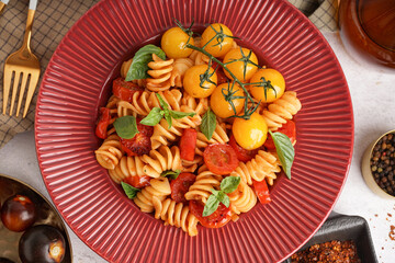 Plate of tasty fusilli pasta with tomatoes and basil on white background