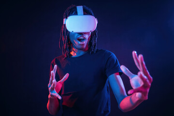 With mouth opened, wow effect. African American guy is with virtual reality glasses in neon room