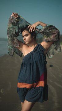 A woman with a colorful scarf striking a dynamic pose on a beach in sunlight