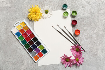 Artist brushes, paints, blank paper sheet and flowers on grey grunge background