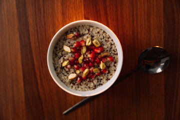 quinoa porridge in a white bowl with pomegranate and nuts, top view