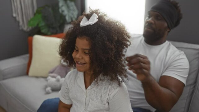 Man styling daughter's curly hair with love in cozy living room at home.