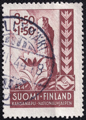 Finnish postage stamp from 1944 promoting national aid, depicting a flower symbolizing renewal, clasped hands representing unity, and arrows signifying resilience.