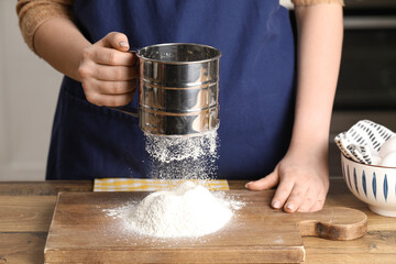 Woman with sieve sifting flour on table in kitchen