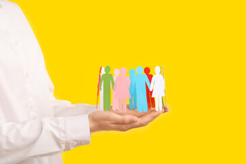 Woman holding paper human figures on yellow background, closeup. Diversity and inclusion concept