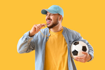 Male sport fan with soccer ball and whistle on yellow background