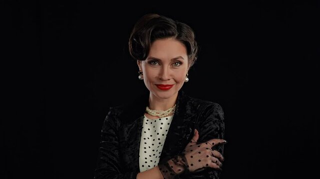 Retro woman actress with pin-up hairstyle and makeup smiles looking and posing at camera, isolated on black background, Slow motion.