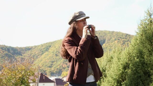 Mid shot of a young Caucasian woman merrily playing an ocarina ceramic flute. The sky and mountain is in the background. Ethnic music on a whistle toy