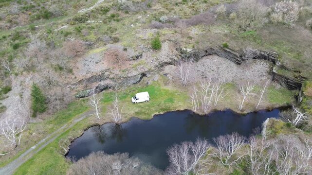Fourgon am&eacute;nag&eacute; au bord d'un etang dans la montagne noire, vue a&eacute;rienne d'un drone avec un van en mouvement.