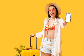 Young female tourist holding mobile phone with blank screen on yellow background
