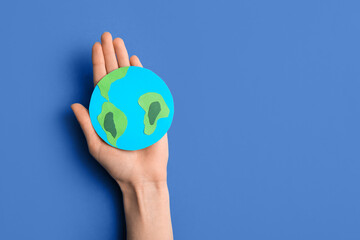 Female hand holding paper planet Earth on blue background. World Earth Day celebration
