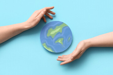 Female hands with paper planet Earth on blue background. World Earth Day celebration