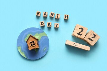 Paper planet Earth, wooden house, words EARTH DAY and calendar with date 22 APRIL on blue background