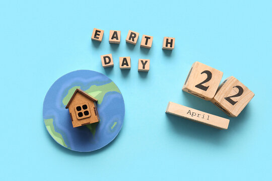 Paper planet Earth, wooden house, words EARTH DAY and calendar with date 22 APRIL on blue background