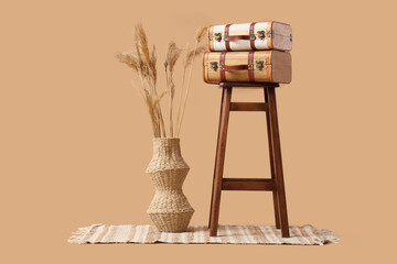 Stylish wooden stool and vintage suitcases and pampas grass on beige background