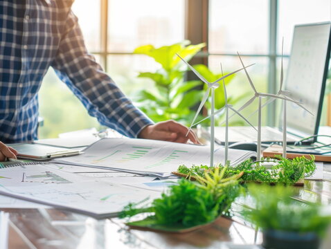 Personne travaillant sur un projet durable, &eacute;cologique avec des &eacute;oliennes de la verdure et de la v&eacute;g&eacute;tation sur son bureau