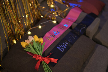 festive bridal party setup with sashes labeled Bride to Be and Bride Team, accompanied by bouquet of tulips tied with red ribbon, and golden