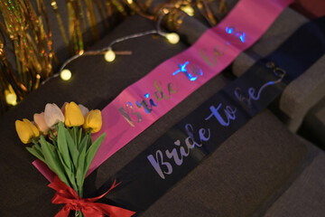 Pink and black Bride to Be sashes with tulip bouquet and festive lights, creating joyful bridal shower atmosphere