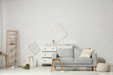 Interior of messy living room with grey sofa, coffee table and overturned houseplant after...