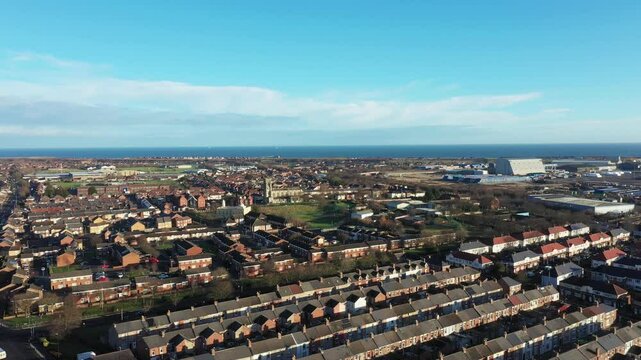 Aerial drone footage of the town of Hartlepool in the UK showing rows of terrace houses and homes with the ocean and harbour in the background on a sunny day in the winter time