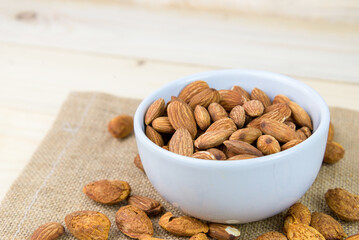 Almonds and almond dry food in white bowl on sack and wooden table background. Almond concept with copyspace. Almond is snack or raw of cook. Healthy food.