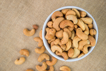 Roasted cashew nut in the white bowl on sack background. Cashew nut is snack or raw of cook. Healthy food. Low calories or diet food. cashew nut with copyspace.