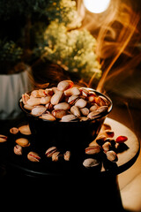 Bowl of pistachios surrounded by shells on a dark table with warm lighting