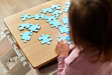 Cute little child girl connecting puzzle pieces on wooden desk in room, top view