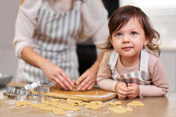 Happy family mother and little child daughter cutting cookies of raw gingerbread dough in kitchen