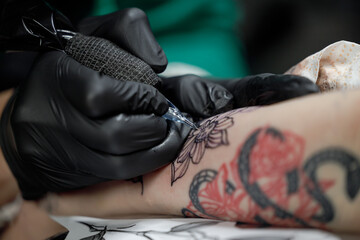 Close up tattoo master professional tattoo artist in black gloves making a rose tattoo on a man's...