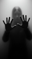 A blurry black-and-white photo of two hands behind foggy glass, creating an eerie atmosphere