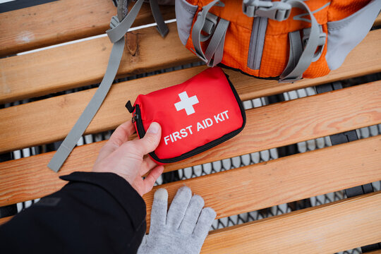 A person is carefully holding a fully stocked first aid kit on a weathered wooden bench, ensuring that it is readily available for any medical emergencies that may arise
