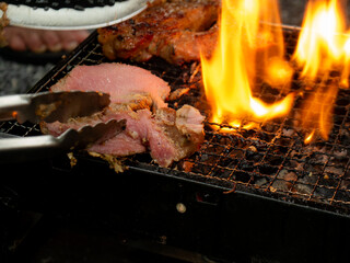 Piece of raw meat placed on grill with flames blazing. Cooked pieces of meat on grill. Hand holding...