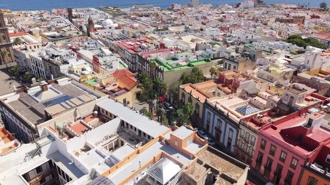 Overhead of Las Palmas colorful rooftops and historic landmarks, surrounded by Atlantic Ocean, dense urban colonial backdrop with Cathedral appearing against skyline