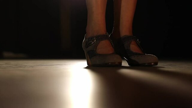 Low POV static shot of flamenco dancer tapping her foot on lit stage