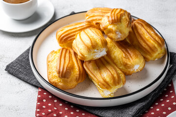French eclair with custard. Profiteroles with cream on a white plate. Side view. Homemade pastries with cream. Light background. Profiteroles with coffee.