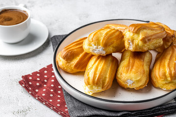 French eclair with custard. Profiteroles with cream on a white plate. Side view. Homemade pastries with cream. Light background. Profiteroles with coffee.