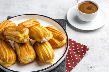 French eclair with custard. Profiteroles with cream on a white plate. Side view. Homemade pastries with cream. Light background. Profiteroles with coffee.