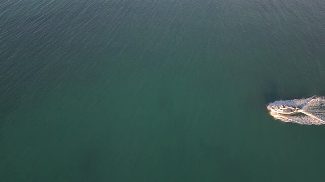 A high-angle aerial video showing a small motorboat cutting swiftly through the open sea, leaving a curved trail of white foam on the deep blue water. 