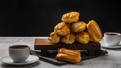 French eclair with custard. Profiteroles with cream on a white plate. Side view. Homemade pastries with cream. Dark background. Profiteroles with coffee.