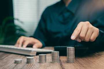 Person Using Calculator for Financial Planning with Stacks of Coins on Wooden Desk, Business concept