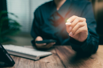 Person in Black Shirt Holding a Small Object While Using a Smartphone on a Wooden Table, Business concept